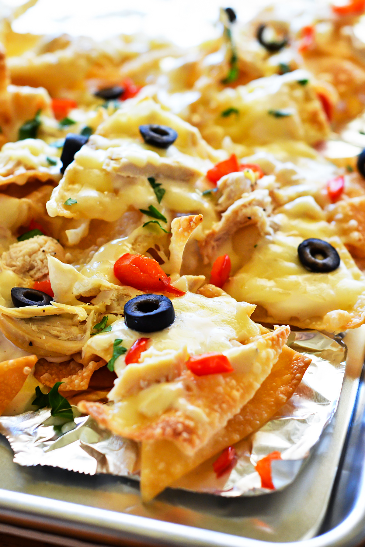 These Italian nachos are made with crispy wontons, shredded chicken, bell peppers, and olives smothered in Alfredo sauce and cheese. Life-in-the-Lofthouse.com