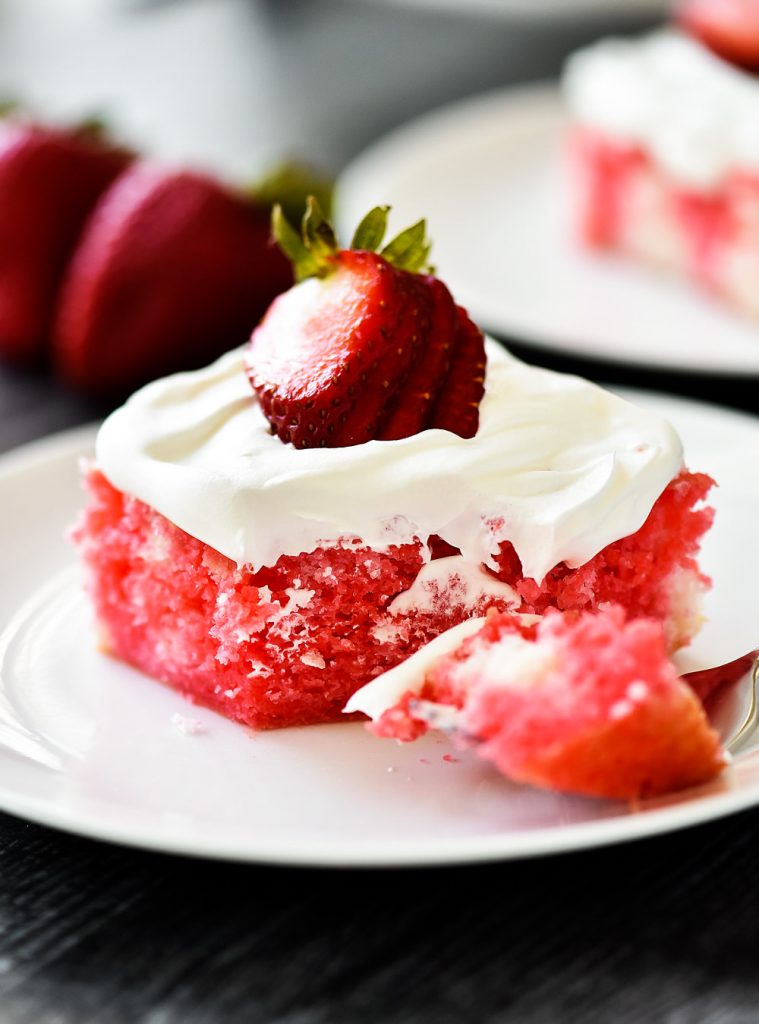 Incredibly light and delicious Strawberry Jello Poke Cake! This white cake is filled with strawberry jello and topped with fresh whipped cream and strawberries.
