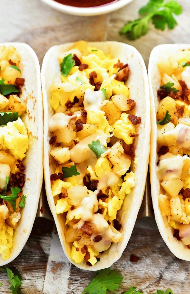 Breakfast Tacos filled with scrambled eggs, crispy bacon, seasoned potatoes and drenched in Queso cheese sauce. Life-in-the-Lofthouse.com