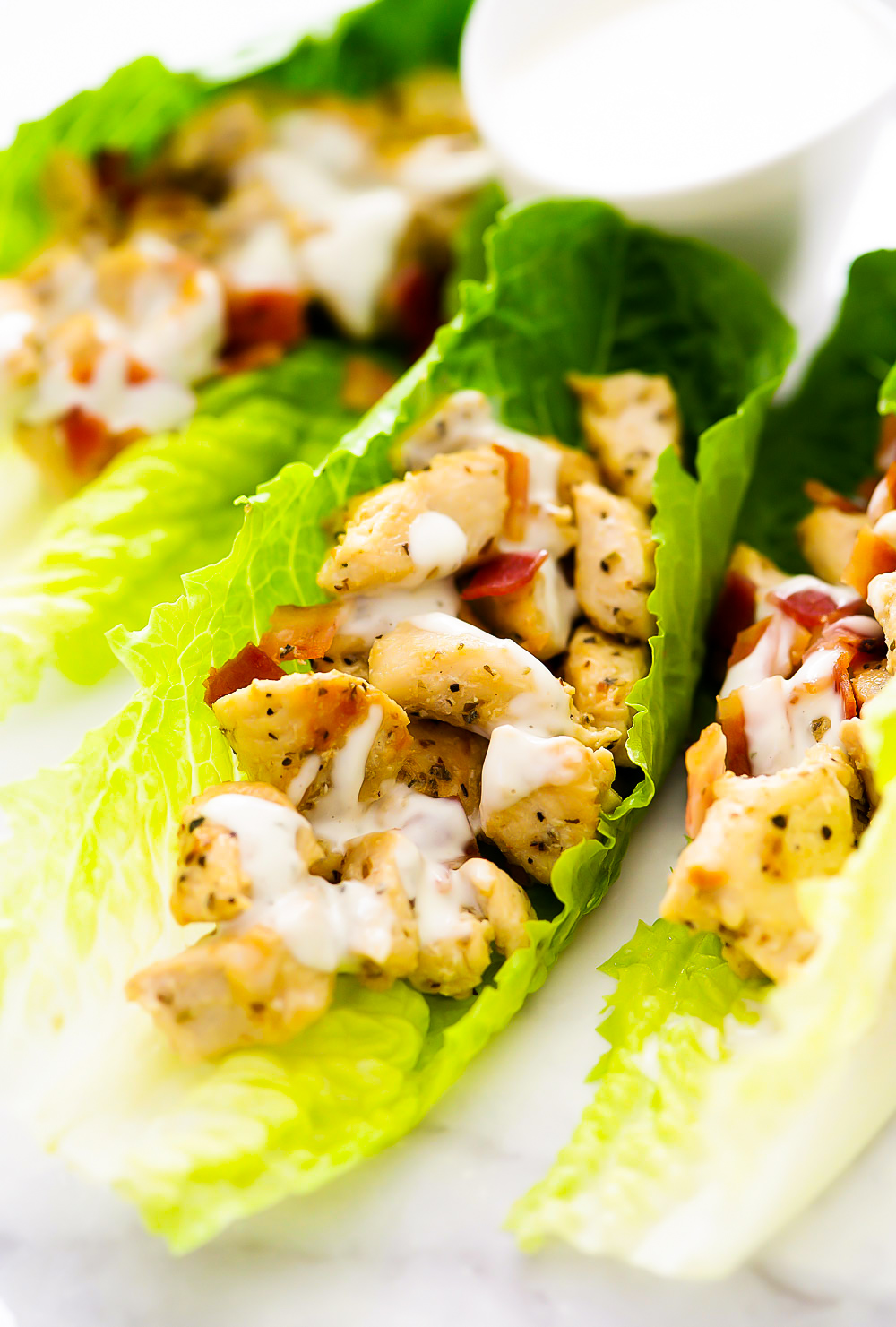 Seasoned chicken and crumbled bacon are filled inside of romaine lettuce leaves. They are topped off with ranch dressing.