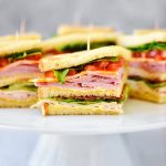 Club Sandwiches are stacked with ham, turkey, cheese, lettuce and tomato with a mustard and mayo mixture.